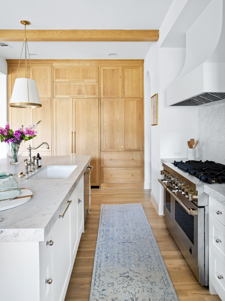 Example of a large transitional l-shaped light wood floor, brown floor and exposed beam open concept kitchen design in Dallas with an undermount sink, shaker cabinets, white cabinets, marble countertops, white backsplash, marble backsplash, paneled appliances, an island and white countertops