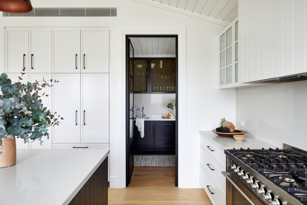 Foto på ett stort lantligt vit kök, med en undermonterad diskho, skåp i shakerstil, vita skåp, marmorbänkskiva, vitt stänkskydd, stänkskydd i marmor, integrerade vitvaror, ljust trägolv, en köksö och brunt golv