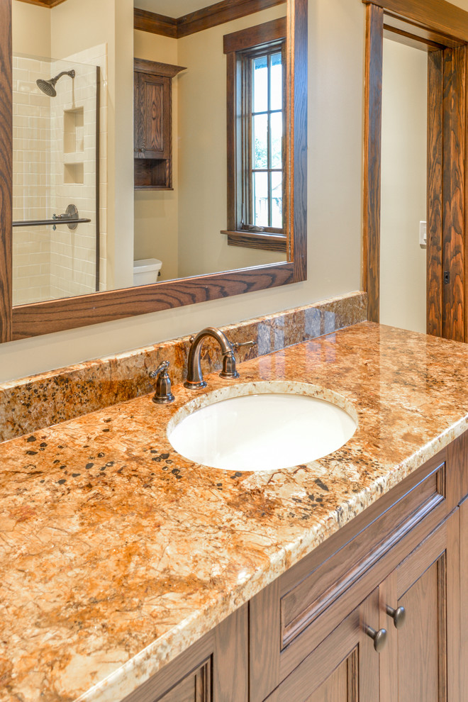 Large mountain style 3/4 beige tile and ceramic tile alcove shower photo with recessed-panel cabinets, dark wood cabinets, beige walls, an undermount sink, granite countertops and brown countertops