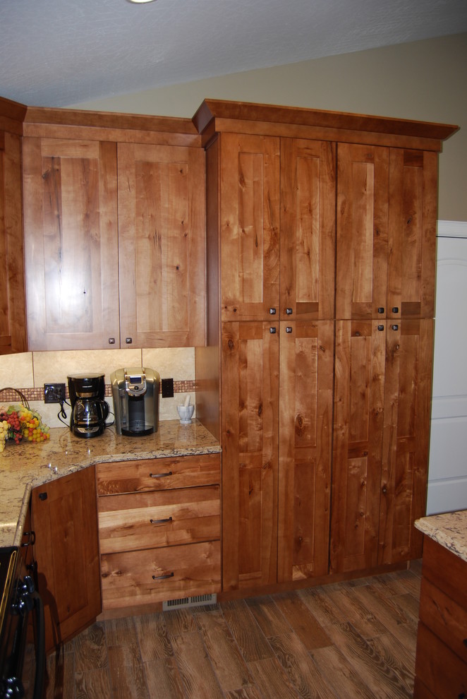Mid-sized mountain style l-shaped porcelain tile and brown floor eat-in kitchen photo with an undermount sink, beaded inset cabinets, medium tone wood cabinets, beige backsplash, porcelain backsplash, quartz countertops, stainless steel appliances and an island
