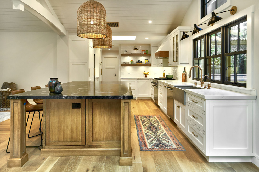 Photo of a large transitional u-shaped open plan kitchen in San Francisco with a farmhouse sink, beaded inset cabinets, white cabinets, quartzite benchtops, white splashback, ceramic splashback, panelled appliances, light hardwood floors, with island, grey floor, white benchtop and vaulted.