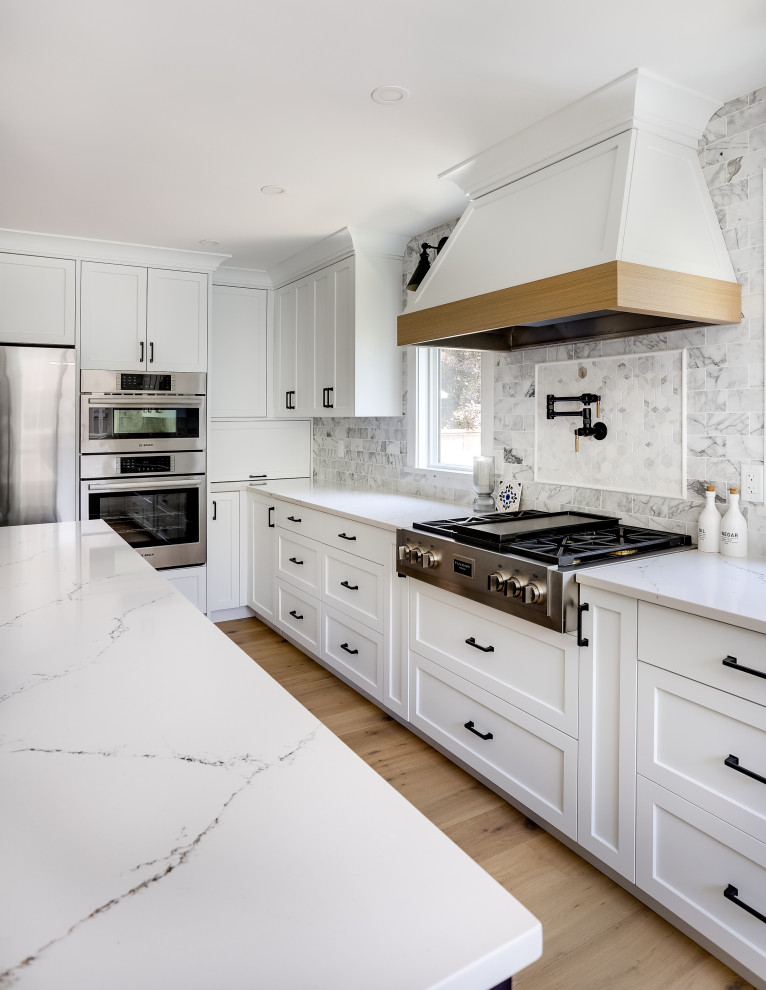 Open concept kitchen - mid-sized transitional l-shaped light wood floor and beige floor open concept kitchen idea in Vancouver with an undermount sink, shaker cabinets, white cabinets, quartz countertops, gray backsplash, marble backsplash, stainless steel appliances, an island and white countertops