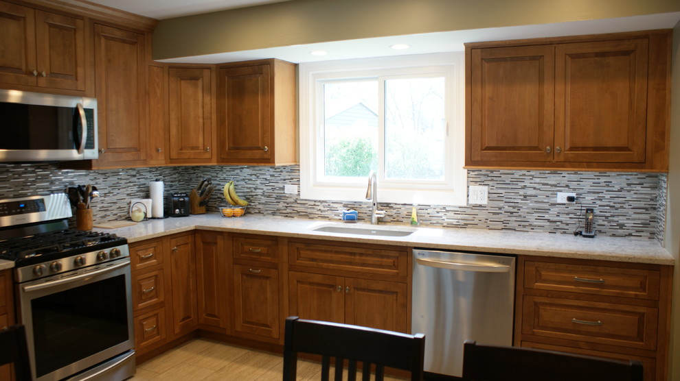 Medium sized traditional l-shaped enclosed kitchen in Chicago with a submerged sink, raised-panel cabinets, medium wood cabinets, engineered stone countertops, multi-coloured splashback, glass sheet splashback, stainless steel appliances, porcelain flooring and no island.