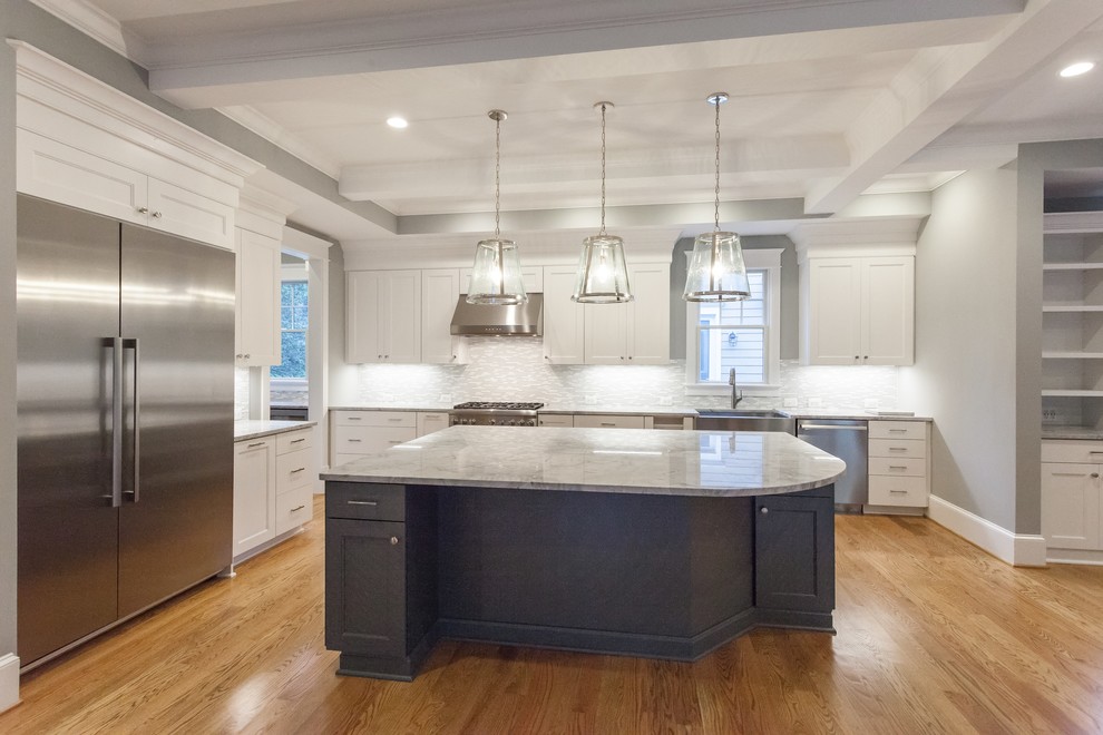 Country l-shaped open plan kitchen in DC Metro with a farmhouse sink, shaker cabinets, white cabinets, quartzite benchtops, grey splashback, glass tile splashback, stainless steel appliances, light hardwood floors, with island, beige floor and grey benchtop.
