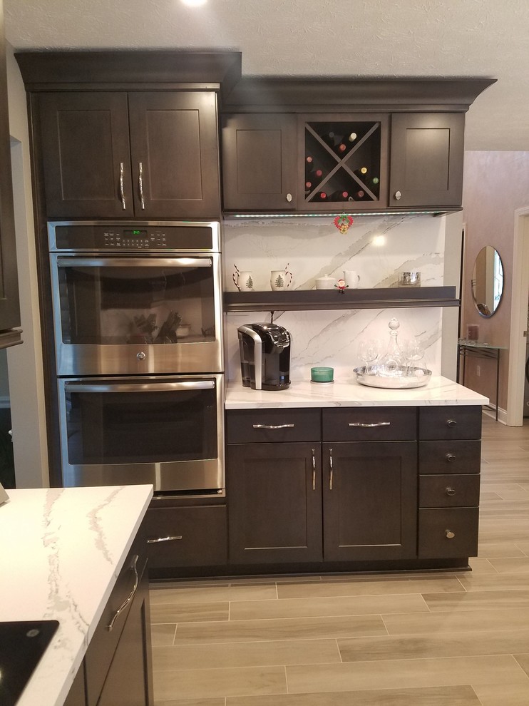 Inspiration for a mid-sized transitional l-shaped porcelain tile and gray floor enclosed kitchen remodel with an undermount sink, raised-panel cabinets, dark wood cabinets, quartz countertops, white backsplash, stone slab backsplash, stainless steel appliances and an island