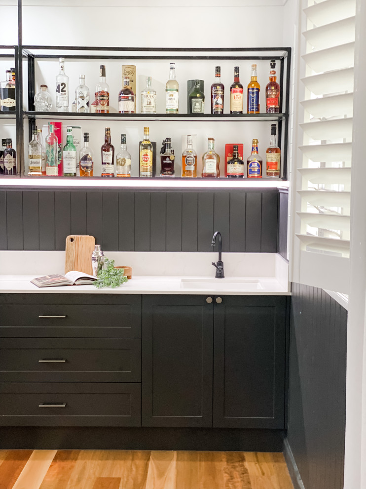 Design ideas for a mid-sized transitional single-wall wet bar in Brisbane with shaker cabinets, black cabinets, white splashback, medium hardwood floors, white benchtop, an undermount sink, quartz benchtops and engineered quartz splashback.