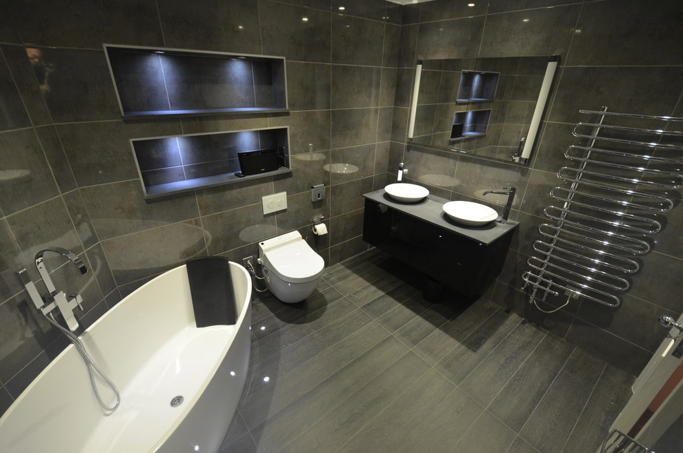 Photo of a mid-sized contemporary wet room bathroom in London with furniture-like cabinets, black cabinets, a freestanding tub, a wall-mount toilet, gray tile, ceramic tile, grey walls, porcelain floors, with a sauna, a wall-mount sink and granite benchtops.