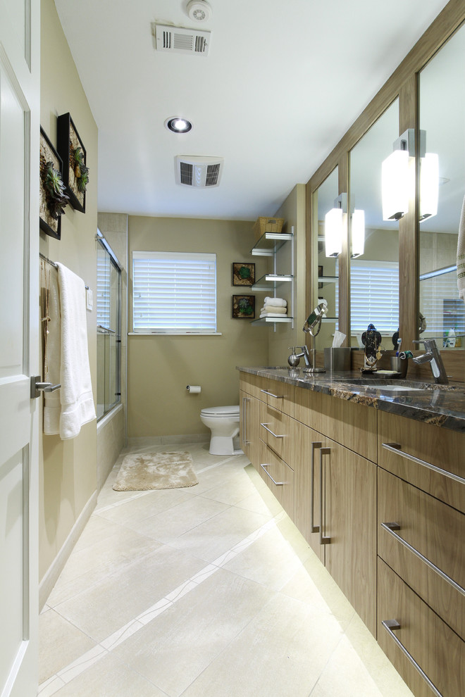 Photo of a small contemporary kids bathroom in Houston with flat-panel cabinets, medium wood cabinets, a drop-in tub, a shower/bathtub combo, a two-piece toilet, beige tile, porcelain tile, beige walls, porcelain floors, granite benchtops and an undermount sink.