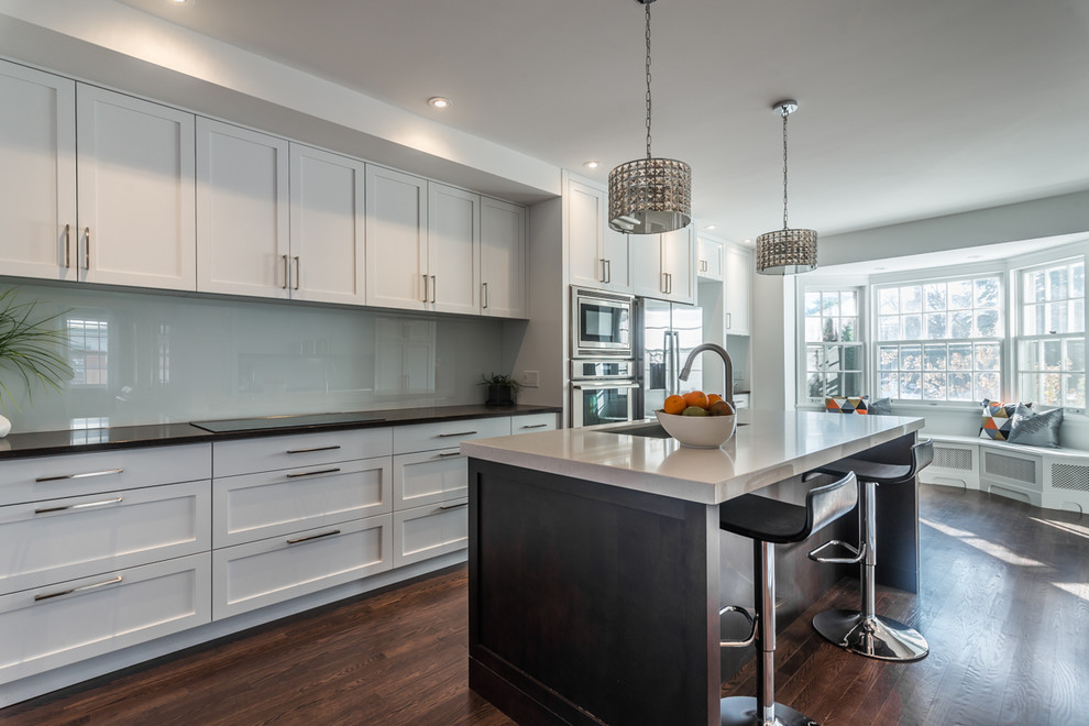 Design ideas for a large contemporary galley eat-in kitchen in Montreal with an undermount sink, shaker cabinets, white cabinets, marble benchtops, white splashback, glass sheet splashback, stainless steel appliances, dark hardwood floors and with island.