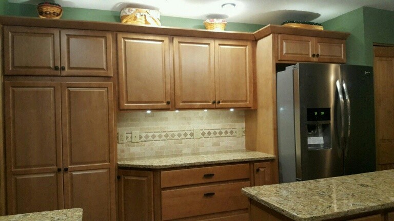Mid-sized mountain style l-shaped ceramic tile and beige floor enclosed kitchen photo with a single-bowl sink, raised-panel cabinets, light wood cabinets, quartz countertops, beige backsplash, ceramic backsplash, stainless steel appliances, an island and beige countertops