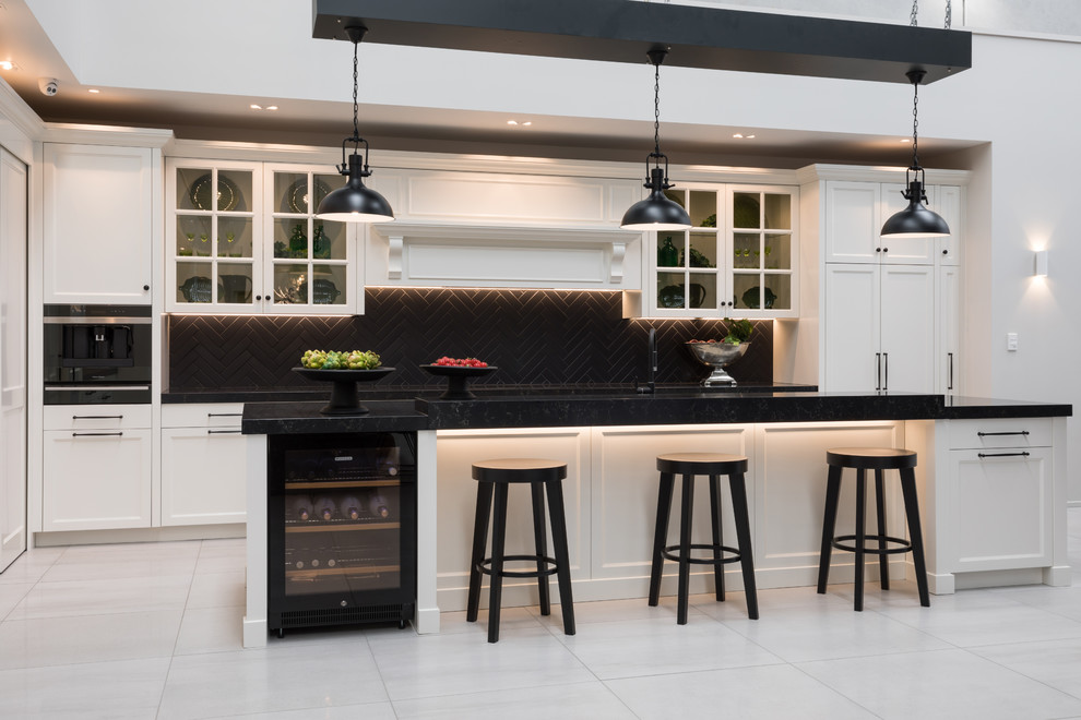 Design ideas for an expansive traditional eat-in kitchen in Auckland with a double-bowl sink, shaker cabinets, white cabinets, quartz benchtops, black splashback, subway tile splashback, stainless steel appliances, porcelain floors, with island, grey floor and black benchtop.