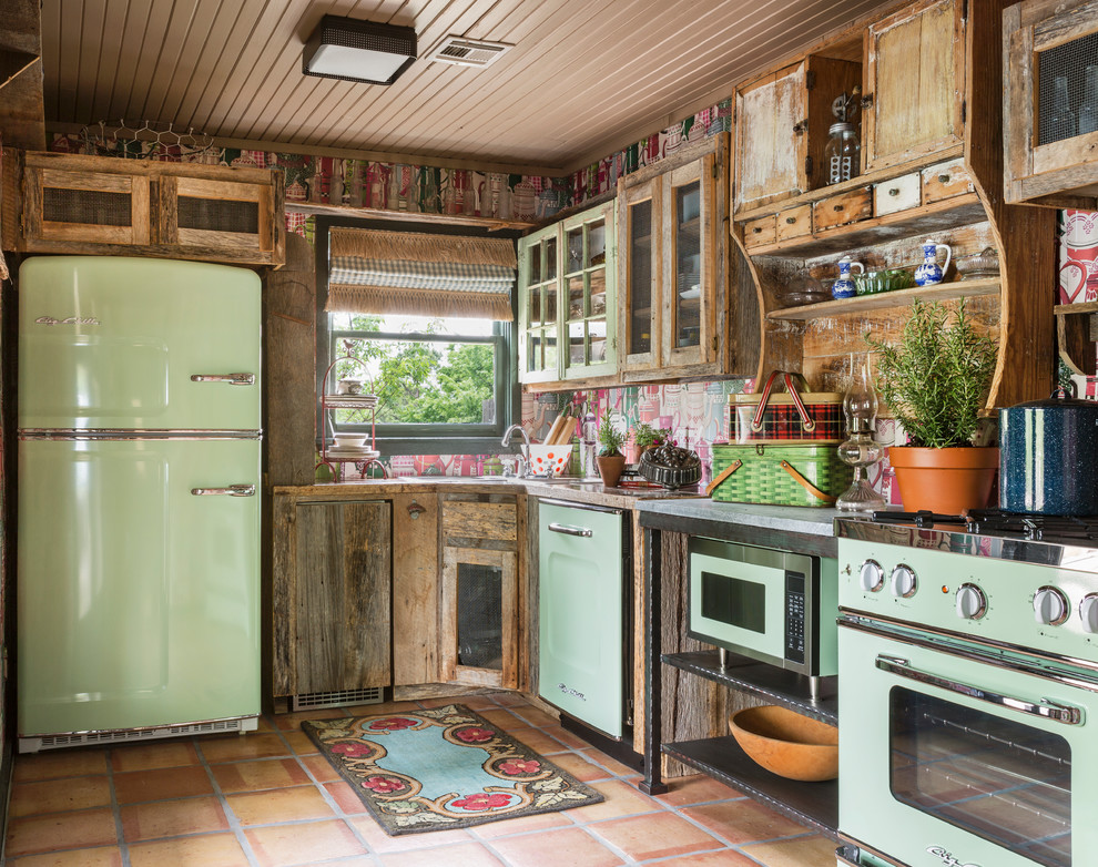 This is an example of a country l-shaped kitchen in Other with glass-front cabinets, distressed cabinets, wood benchtops, multi-coloured splashback, coloured appliances and terra-cotta floors.