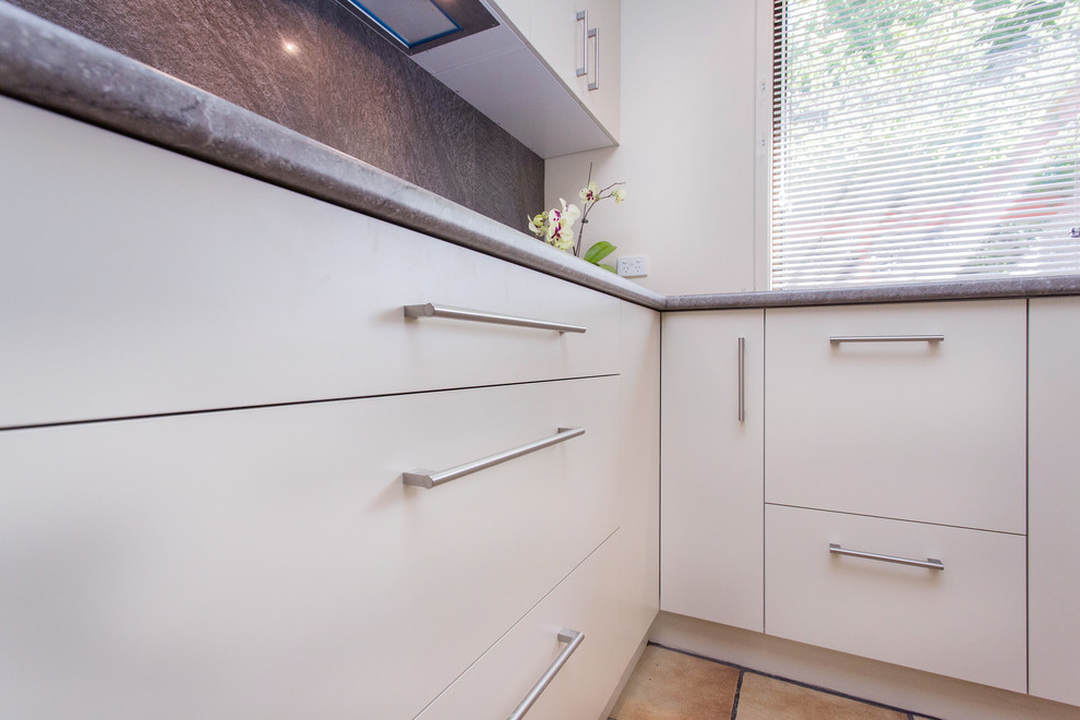 This is an example of a mid-sized contemporary u-shaped eat-in kitchen in Other with a drop-in sink, flat-panel cabinets, white cabinets, laminate benchtops, grey splashback, ceramic splashback, stainless steel appliances, ceramic floors, a peninsula, brown floor and grey benchtop.