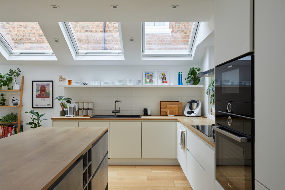 This is an example of a medium sized contemporary grey and brown l-shaped kitchen in London with a single-bowl sink, louvered cabinets, wood worktops, white splashback, metro tiled splashback, light hardwood flooring, an island, brown floors and brown worktops.