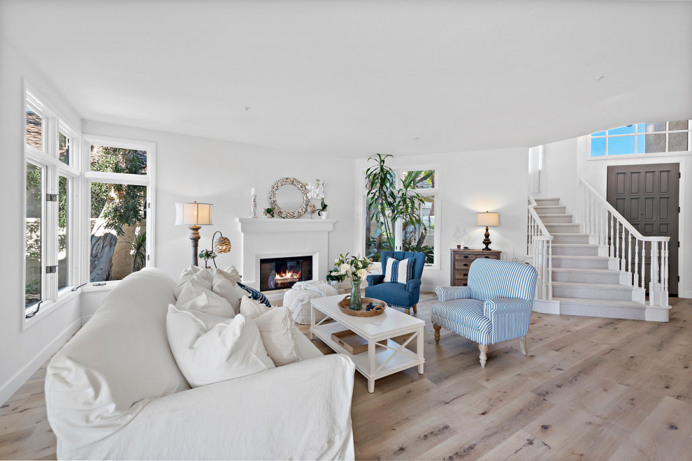 Inspiration for a mid-sized beach style formal open concept living room in Orange County with white walls, vinyl floors, a standard fireplace, a plaster fireplace surround, no tv and beige floor.