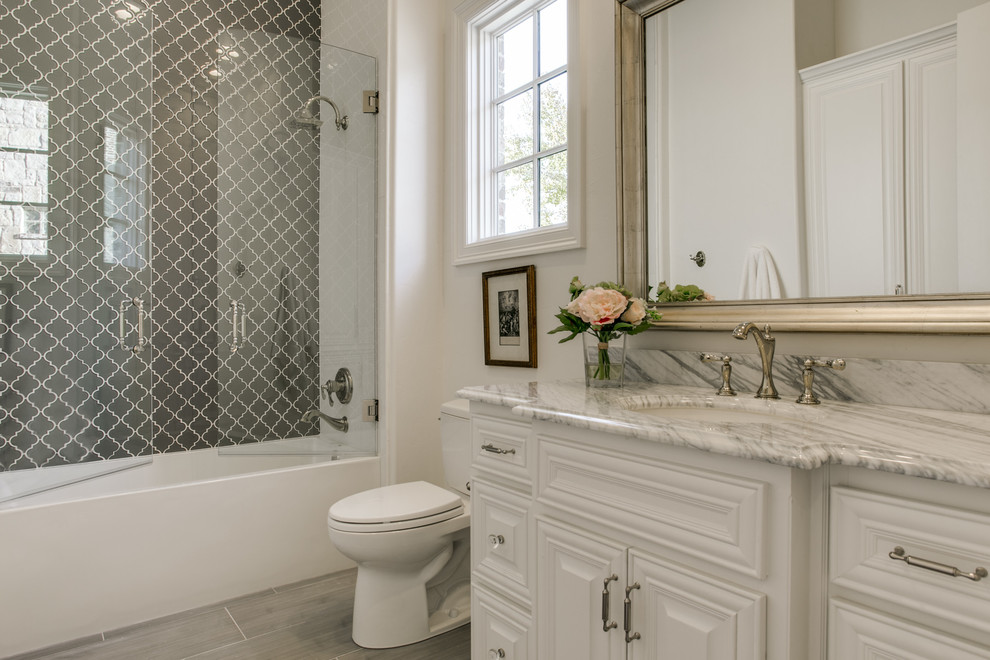 Photo of a small transitional kids bathroom in Dallas with raised-panel cabinets, white cabinets, a shower/bathtub combo, a two-piece toilet, gray tile, glass sheet wall, white walls, porcelain floors, an undermount sink and marble benchtops.