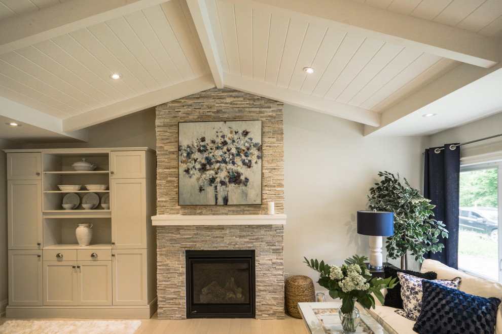 Photo of a mid-sized transitional open concept living room in Toronto with grey walls, light hardwood floors, a standard fireplace, a stone fireplace surround, beige floor and vaulted.