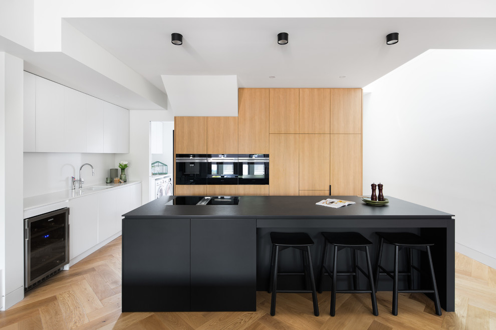Design ideas for a mid-sized contemporary galley eat-in kitchen in Melbourne with a drop-in sink, flat-panel cabinets, medium wood cabinets, concrete benchtops, black appliances, light hardwood floors, with island, brown floor and black benchtop.
