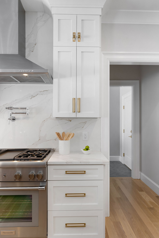 Open concept kitchen - huge transitional light wood floor and brown floor open concept kitchen idea in Boston with an undermount sink, shaker cabinets, white cabinets, quartz countertops, white backsplash, quartz backsplash, stainless steel appliances, an island and white countertops