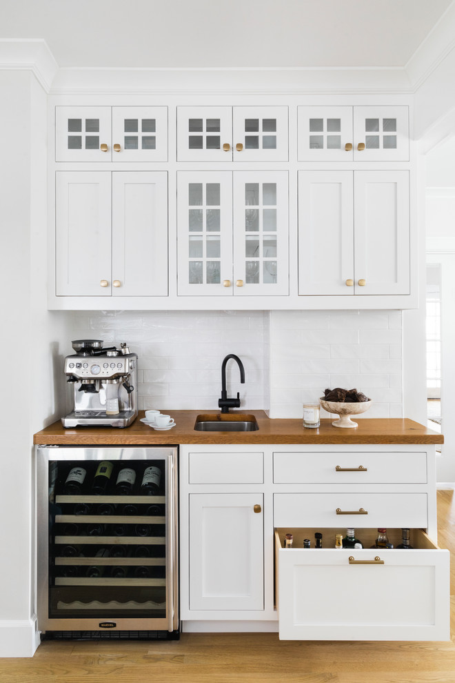 This is an example of a mid-sized traditional single-wall wet bar in Boston with an undermount sink, white cabinets, wood benchtops, white splashback, subway tile splashback, medium hardwood floors, brown benchtop and shaker cabinets.