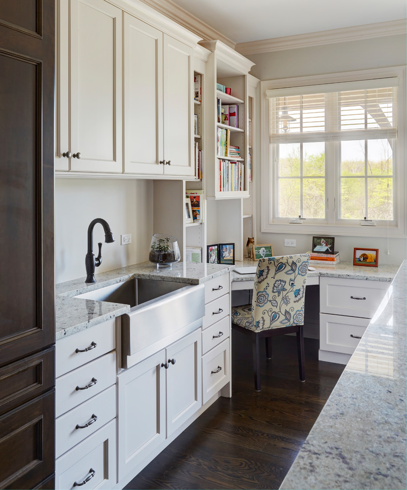 Inspiration for a mid-sized traditional u-shaped utility room in Chicago with a farmhouse sink, shaker cabinets, white cabinets, granite benchtops, white walls, dark hardwood floors, a concealed washer and dryer, brown floor and multi-coloured benchtop.
