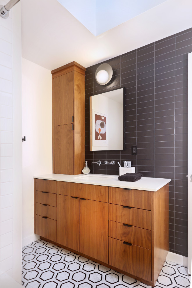 This is an example of a midcentury bathroom in Seattle with flat-panel cabinets, medium wood cabinets, black tile, white walls, an undermount sink, multi-coloured floor, white benchtops, a single vanity and a built-in vanity.
