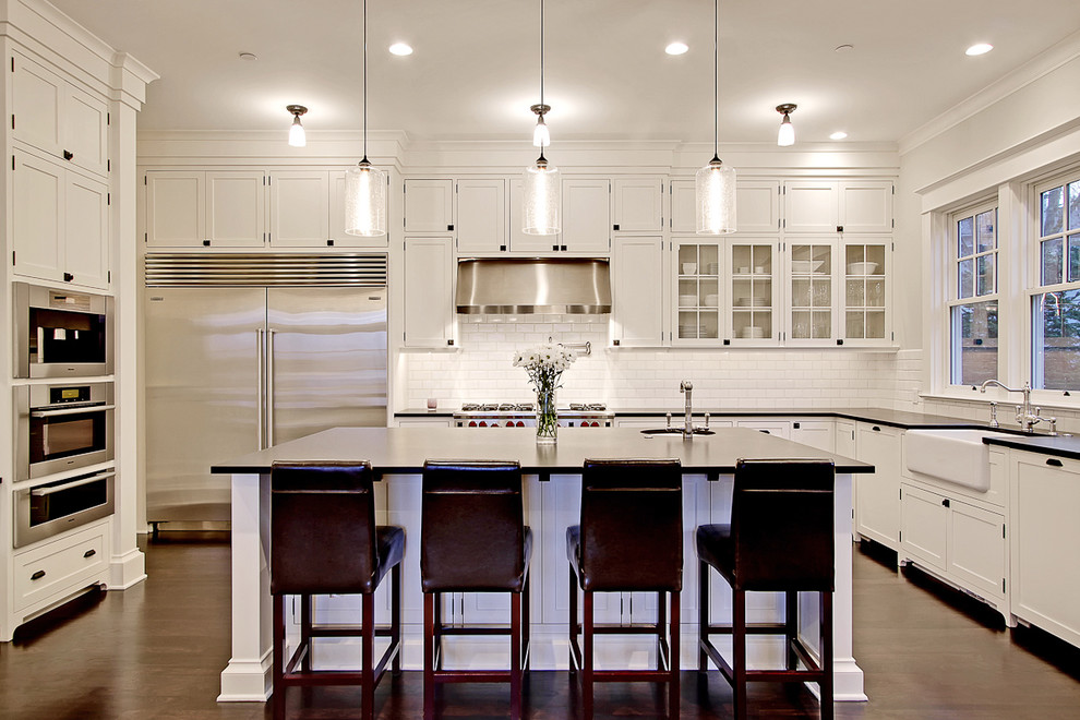 Large traditional u-shaped kitchen in Seattle with shaker cabinets, stainless steel appliances, subway tile splashback, a farmhouse sink, white cabinets, granite benchtops, white splashback, dark hardwood floors and with island.