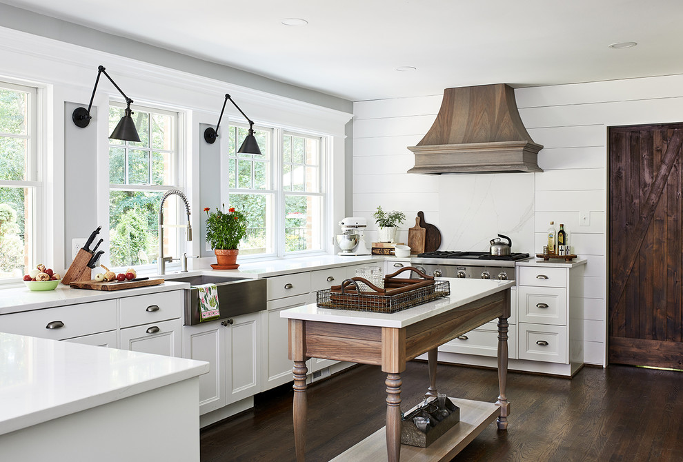This is an example of a mid-sized country u-shaped eat-in kitchen in DC Metro with white splashback, stainless steel appliances, dark hardwood floors, with island, white benchtop, a farmhouse sink, recessed-panel cabinets, white cabinets and brown floor.