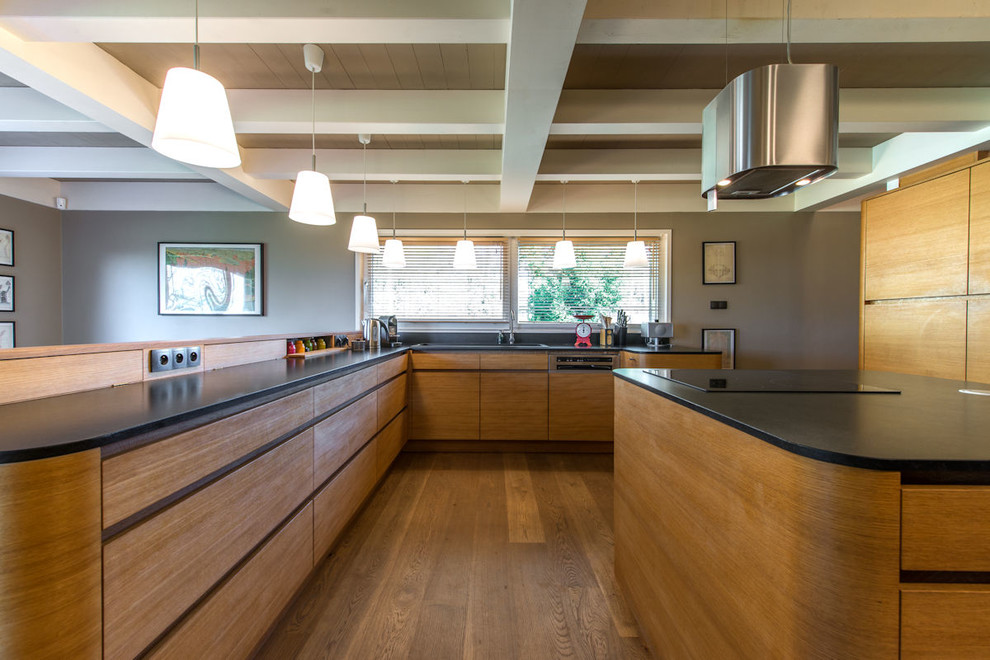 Photo of a large scandinavian u-shaped eat-in kitchen in Lyon with an undermount sink, light wood cabinets, granite benchtops, black splashback, stainless steel appliances, light hardwood floors, with island and black benchtop.