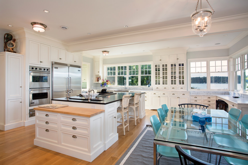 Inspiration for a large beach style u-shaped eat-in kitchen in Seattle with recessed-panel cabinets, white cabinets, granite benchtops, white splashback, stone tile splashback, stainless steel appliances, medium hardwood floors and with island.
