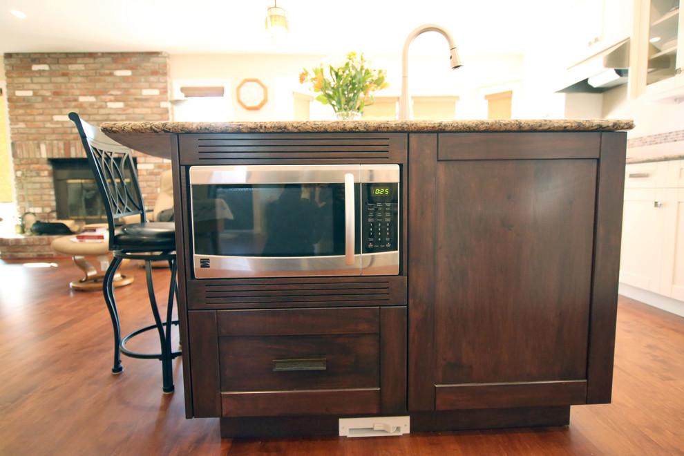 Mid-sized transitional l-shaped medium tone wood floor and brown floor open concept kitchen photo in Calgary with an undermount sink, shaker cabinets, white cabinets, granite countertops, white backsplash, mosaic tile backsplash, stainless steel appliances, an island and beige countertops