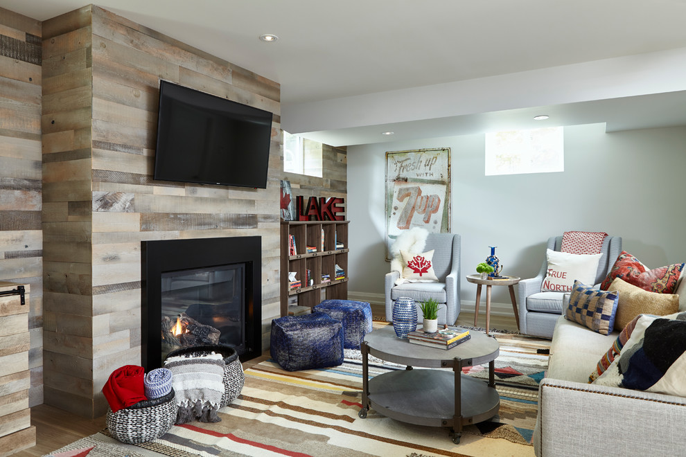 Beach style basement in Toronto with grey walls, medium hardwood floors, a standard fireplace, a wood fireplace surround and brown floor.