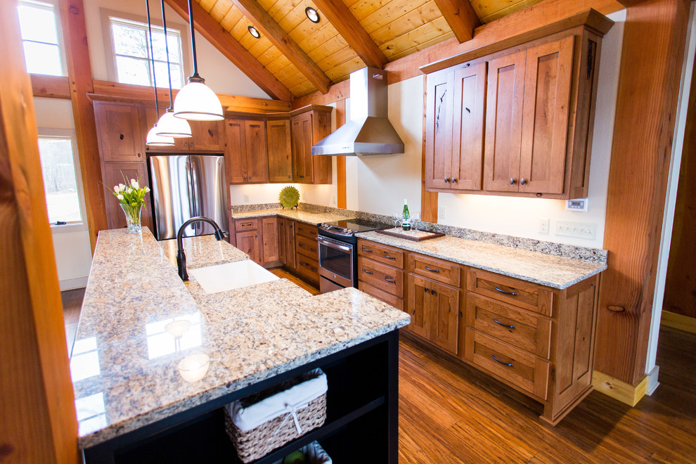 Large mountain style l-shaped medium tone wood floor open concept kitchen photo with a farmhouse sink, shaker cabinets, medium tone wood cabinets, granite countertops, stainless steel appliances and an island