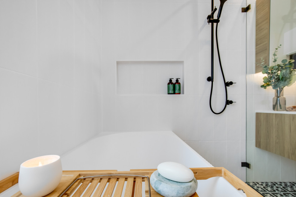 Inredning av ett modernt stort vit vitt badrum, med möbel-liknande, skåp i ljust trä, en öppen dusch, en toalettstol med hel cisternkåpa, vit kakel, vita väggar, ett fristående handfat, flerfärgat golv och med dusch som är öppen