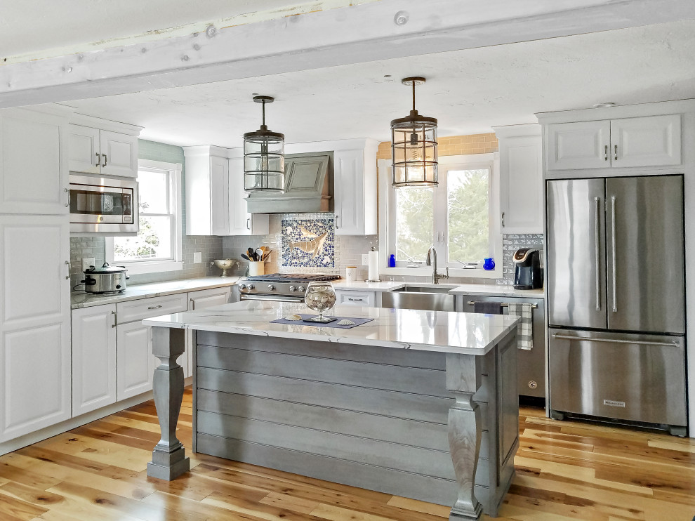 Mid-sized transitional l-shaped kitchen in Boston with a farmhouse sink, raised-panel cabinets, white cabinets, grey splashback, stainless steel appliances, with island, brown floor and grey benchtop.