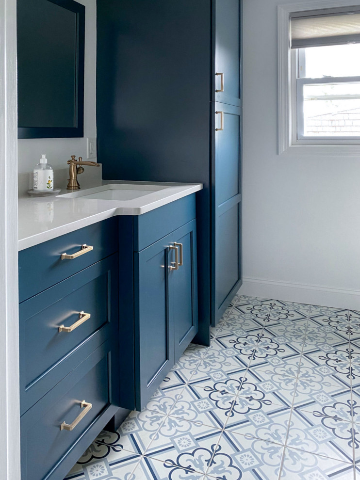 This is an example of a traditional bathroom in Boston with raised-panel cabinets, blue cabinets, an alcove shower, a two-piece toilet, white walls, porcelain flooring, a submerged sink, engineered stone worktops, blue floors, a hinged door, white worktops, a single sink and a built in vanity unit.