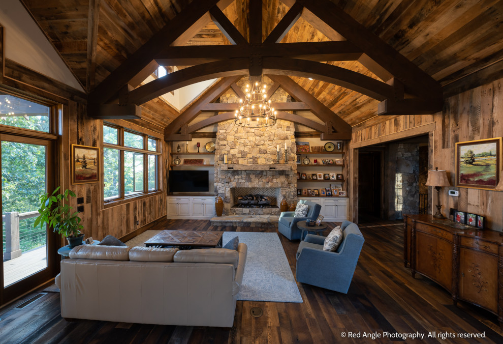 Mid-sized country open concept family room in Other with dark hardwood floors, a standard fireplace, a stone fireplace surround, a corner tv, brown floor, exposed beam and wood walls.