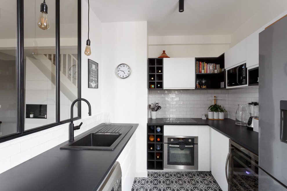 Small scandinavian u-shaped open plan kitchen in Paris with a drop-in sink, flat-panel cabinets, white cabinets, white splashback, subway tile splashback, black appliances, black benchtop, solid surface benchtops, cement tiles, no island and grey floor.