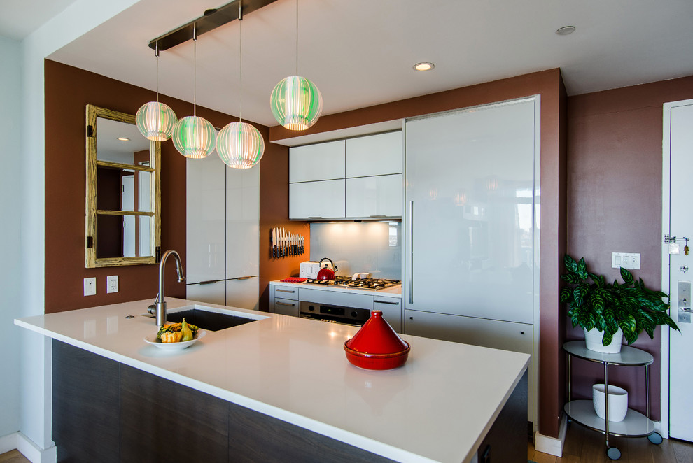 Design ideas for a small contemporary galley open plan kitchen in New York with an undermount sink, glass-front cabinets, white cabinets, quartz benchtops, orange splashback, white appliances, light hardwood floors and with island.