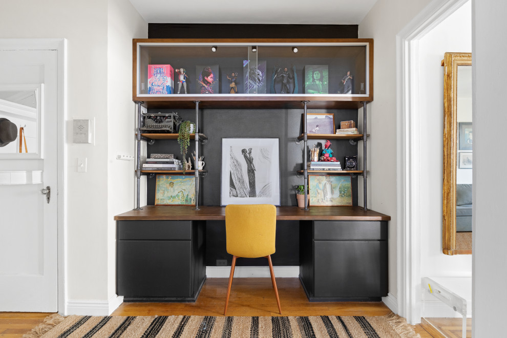 Inspiration for a small eclectic home office in New York with black walls, light hardwood floors and a built-in desk.