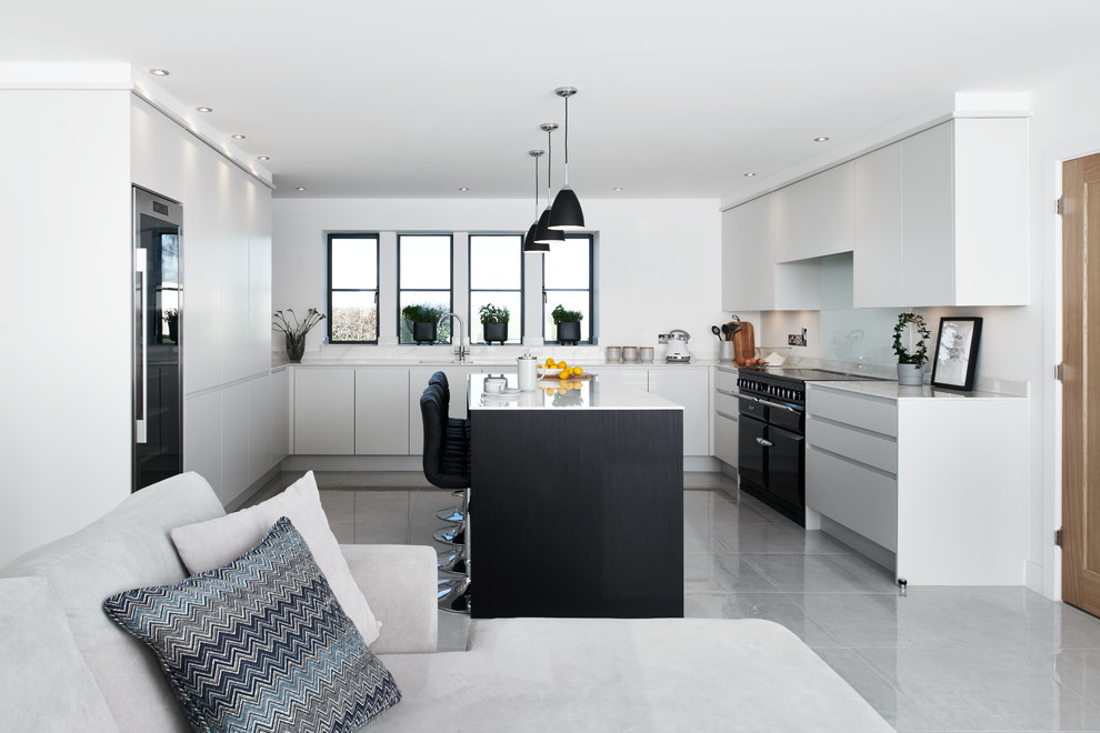 This is an example of a modern u-shaped kitchen in Wiltshire with a single-bowl sink, flat-panel cabinets, solid surface benchtops, white splashback, glass sheet splashback, black appliances, porcelain floors, with island, grey floor and white benchtop.