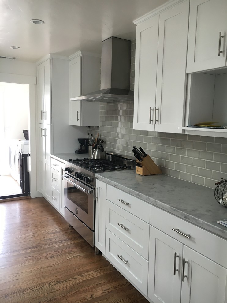 Mid-sized transitional l-shaped eat-in kitchen in San Francisco with a farmhouse sink, shaker cabinets, white cabinets, marble benchtops, grey splashback, subway tile splashback, stainless steel appliances, medium hardwood floors and no island.