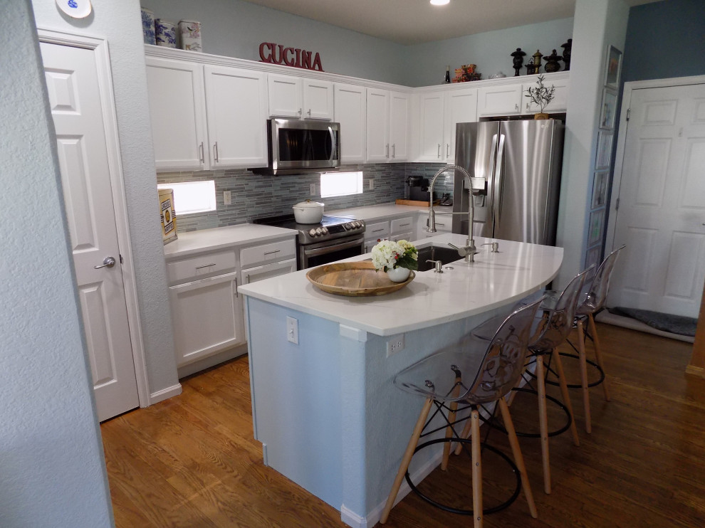 Bild på ett litet funkis vit vitt u-kök, med en undermonterad diskho, luckor med infälld panel, vita skåp, bänkskiva i kvartsit, blått stänkskydd, stänkskydd i glaskakel, rostfria vitvaror, målat trägolv, en köksö och gult golv