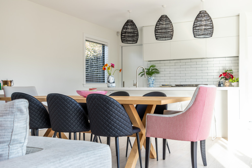 This is an example of a medium sized modern dining room in Christchurch with white walls, light hardwood flooring, a standard fireplace and a concrete fireplace surround.