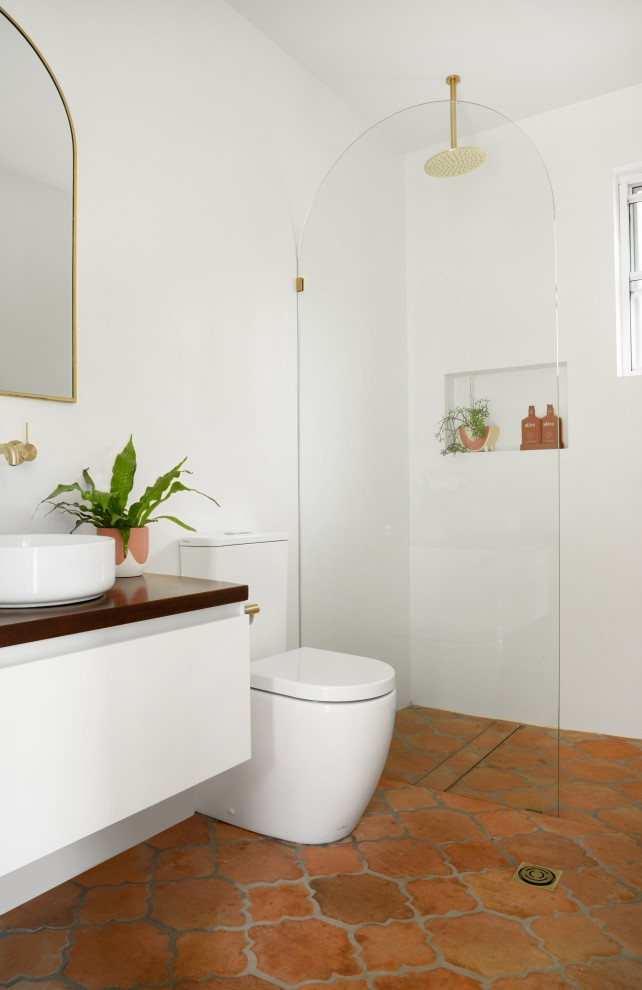 Aménagement d'une salle de bain méditerranéenne de taille moyenne avec un placard à porte plane, des portes de placard blanches, une douche ouverte, un carrelage blanc, un mur blanc, tomettes au sol, une vasque, un plan de toilette en bois, un sol orange, un plan de toilette marron, meuble simple vasque et meuble-lavabo suspendu.