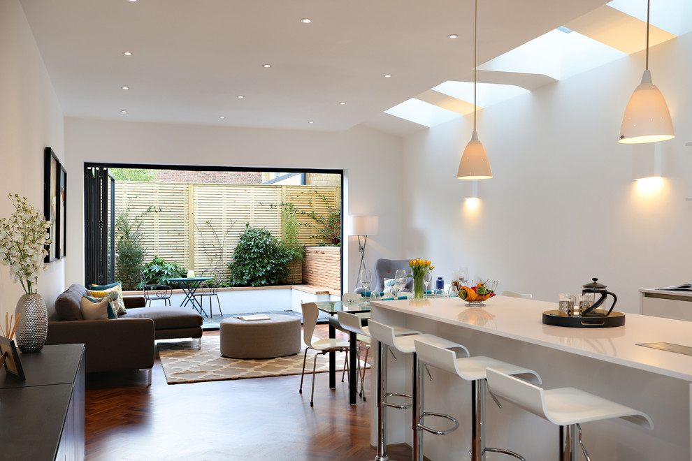 Expansive contemporary eat-in kitchen in London with a drop-in sink, flat-panel cabinets, white cabinets, quartz benchtops, panelled appliances, dark hardwood floors, a peninsula and brown floor.