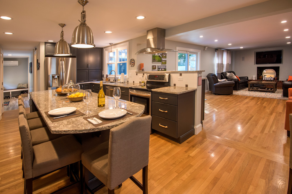 This is an example of a large modern u-shaped eat-in kitchen in Boston with a drop-in sink, flat-panel cabinets, black cabinets, granite benchtops, stainless steel appliances, medium hardwood floors, with island, brown floor and multi-coloured benchtop.