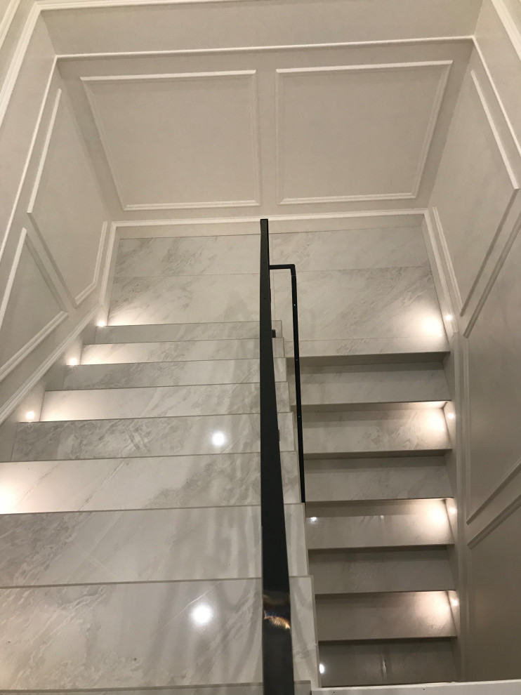 Стильный дизайн: огромная изогнутая лестница в викторианском стиле с металлическими перилами, мраморными ступенями, подступенками из мрамора и панелями на стенах - последний тренд