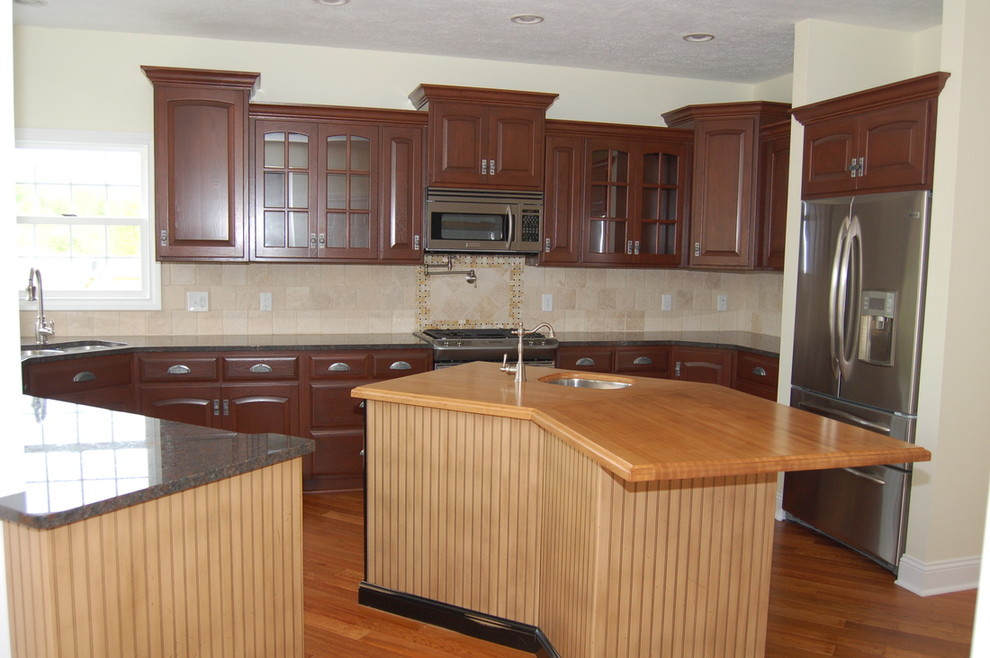 Example of a transitional light wood floor kitchen design with a double-bowl sink, raised-panel cabinets, medium tone wood cabinets, granite countertops, beige backsplash, ceramic backsplash, stainless steel appliances and an island