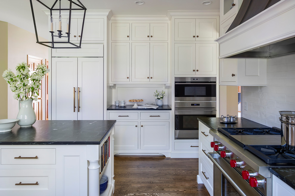 Design ideas for a mid-sized traditional l-shaped open plan kitchen in Minneapolis with a single-bowl sink, recessed-panel cabinets, white cabinets, granite benchtops, white splashback, ceramic splashback, stainless steel appliances, medium hardwood floors, with island and brown floor.